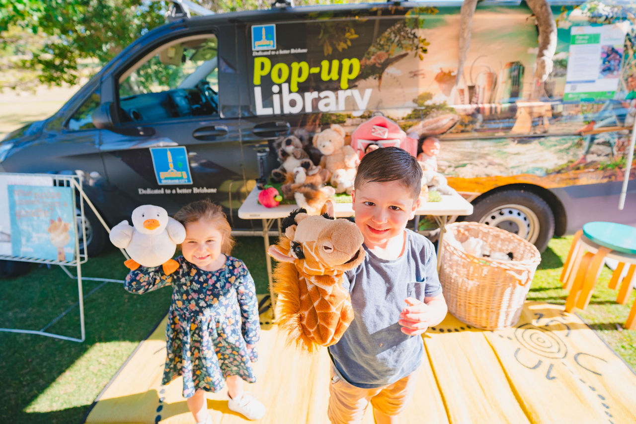 Two children with puppets in front of the Pop-up Library van at a Green Heart Fair event.