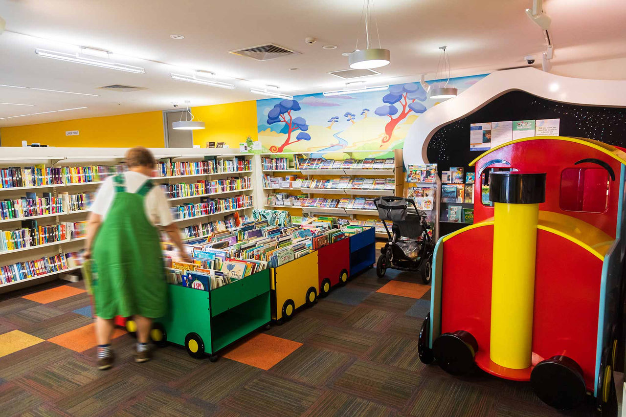 A woman in a green smock dress browsing childrens' books at Fairfield Library.