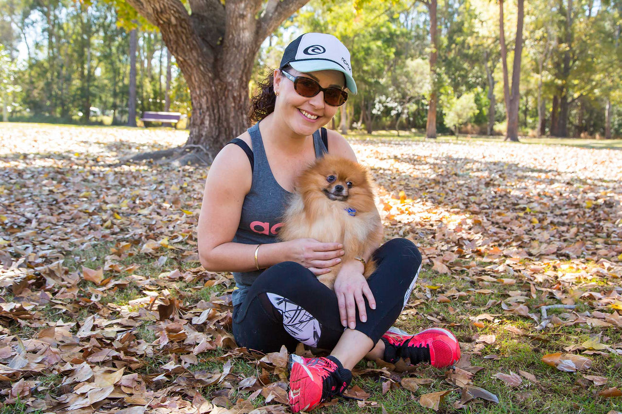 Woman sitting in a park holding a small dog in her lap.