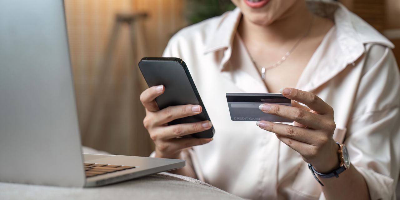 Close up the hands of a woman making a card payment on mobile in front of a laptop.