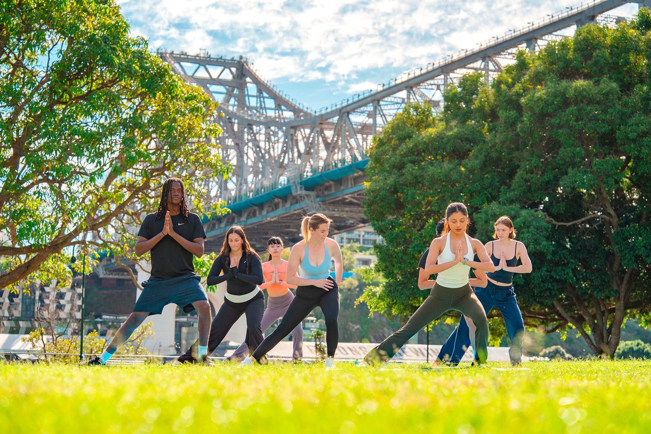A group of people doing yoga in a park near the Story Bridge
