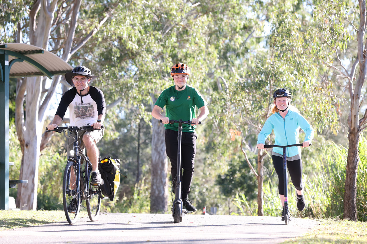 3 people riding bikes and scooters on a pathway in Rocks Riverside Park.