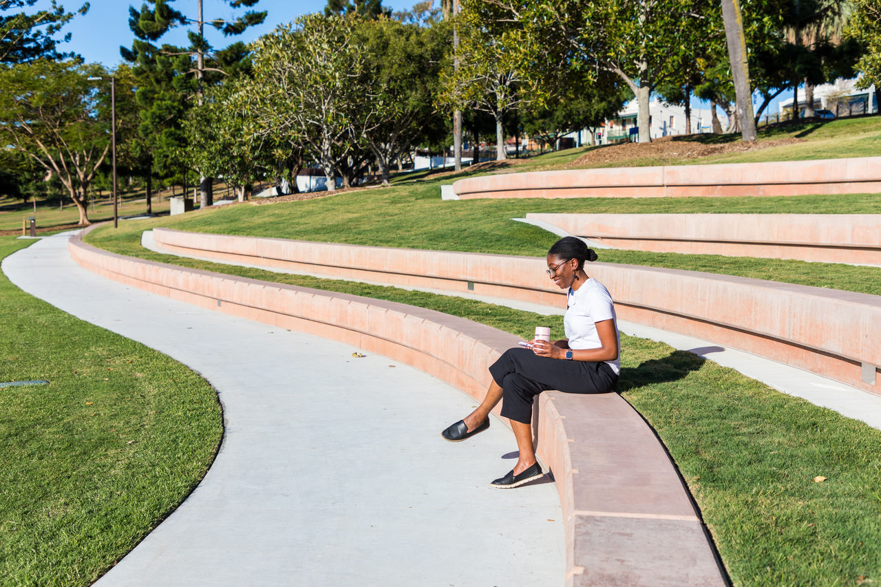 Woman drinking a takeaway coffee while sitting on the tiered seating at Spring Hill Common in Victoria Park.