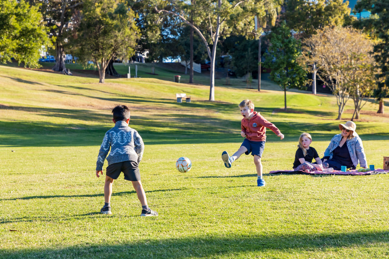 Boys kicking a soccer ball while on a family picnic on the lawn at Spring Hill Common in Victoria Park.