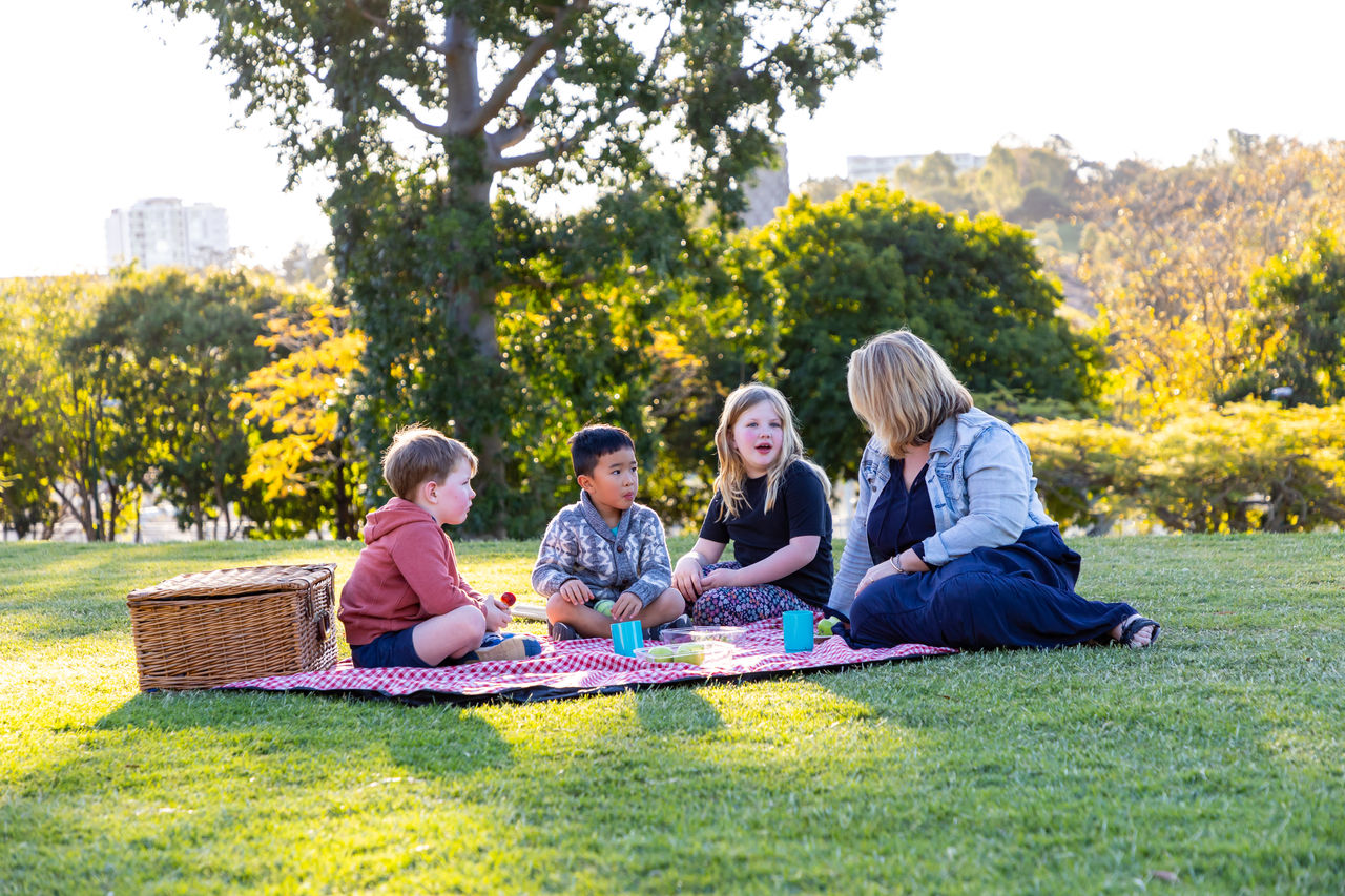 A woman with 3 children enjoying a picnic on the lawn at Spring Hill Common, in Victoria Park.
