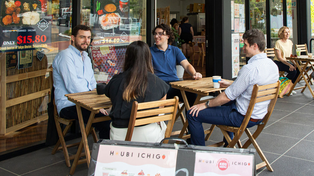 Four people sitting at tables outside a food shop.