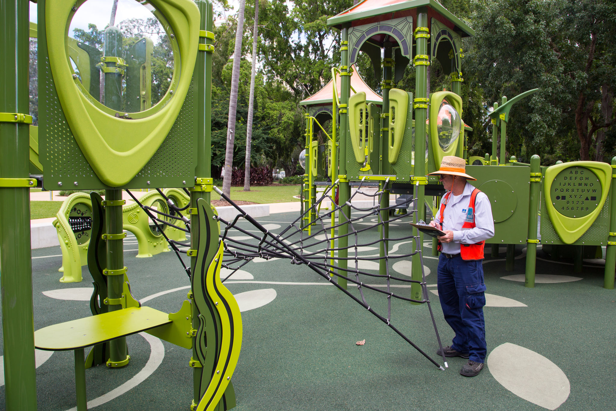 A Council officer with a bright orange vest inspecting a park playground.
