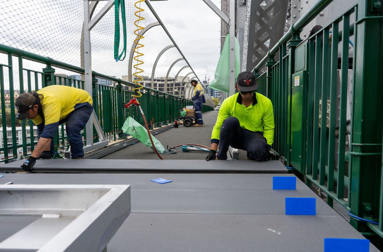 Two people are laying paving along a pathway on a bridge.