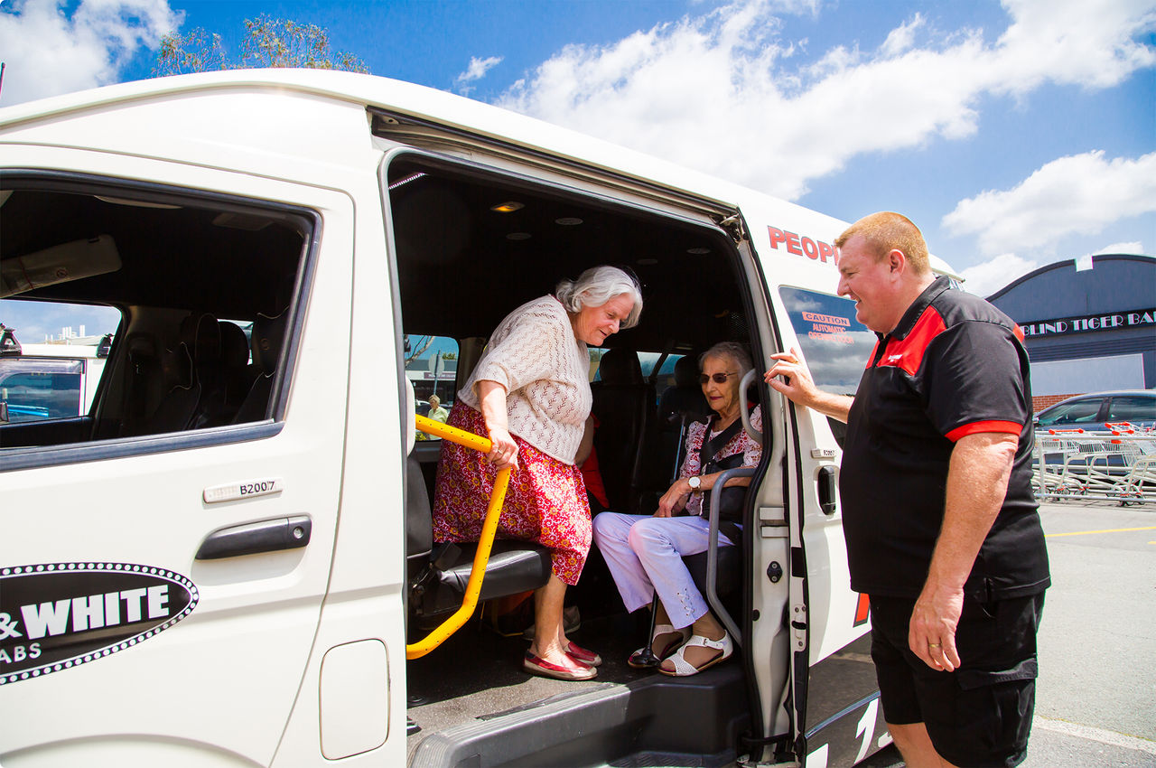 Black & White male cab drive helping an elderly female passenger step out of a taxi.