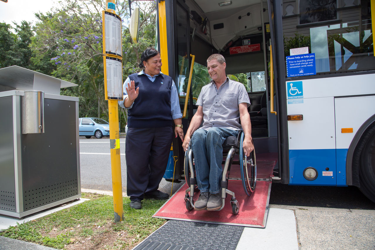 Female bus driver helping a man in a wheelchair exit a bus via the front door.