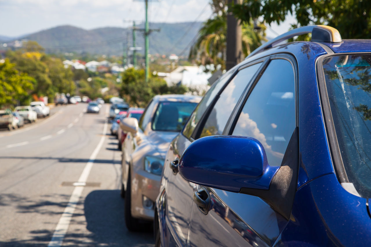 A row of parked cars lines a quiet suburban street on a sunny day.