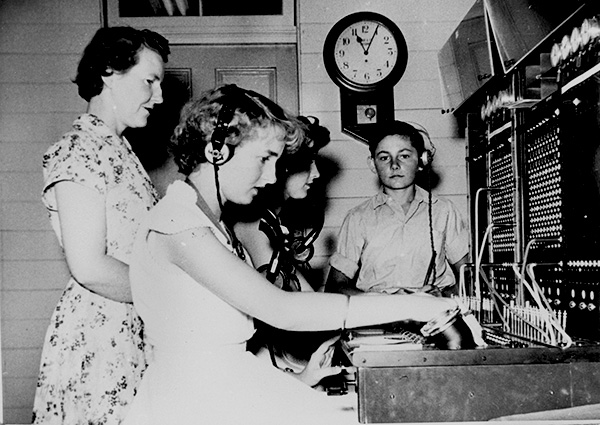 Historic image of a manual telephone exchange with works sitting at the switchboard