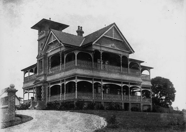This black and white photograph shows Home, also known as Lamb House, circa 1904. The 2-story house is grand with prominent gables, and ornate verandahs and decorative arches surrounding it at each level. There is a wide path leading to the house in the foreground on the left, and a grass lawn in front of the house to the right.