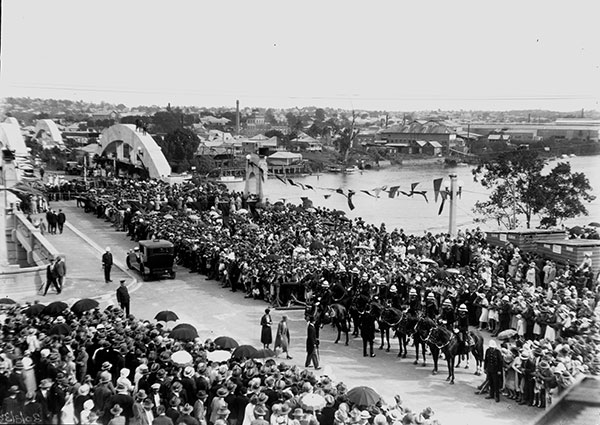 This black and white photograph shows a huge crowd gathered on and around William Jolly Bridge for its official opening on 30 March 1932. There are so many people that most of the bridge and road surface cannot be seen. Well-dressed men and women are wearing hats and there are strings of flagged bunting overhead.