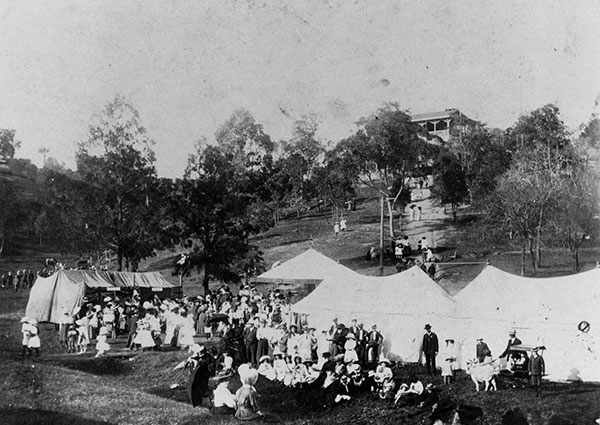 This is a black and white photograph of a fair held at Dutton Park in 1909 by the local lodge of the International Order of Good Templars. It shows a crowd of people standing around white pavilion tents in a park with grassy hills and trees.